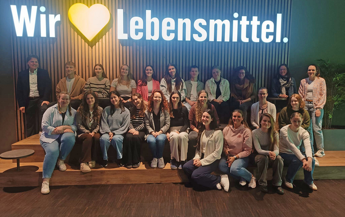 WP-Exkursion zu Edeka Gruppenfot von WP6-Studierende unter dem leuchtenden Edeka-Schriftzug "Wir lieben Lebensmittel"