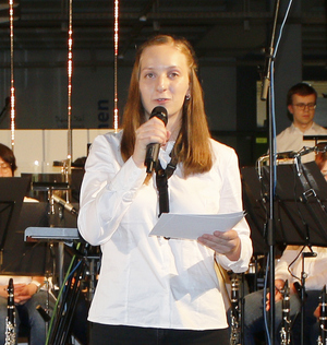 Annika Tetens steht mit Mikrofon in der Hand vor dem Orchester