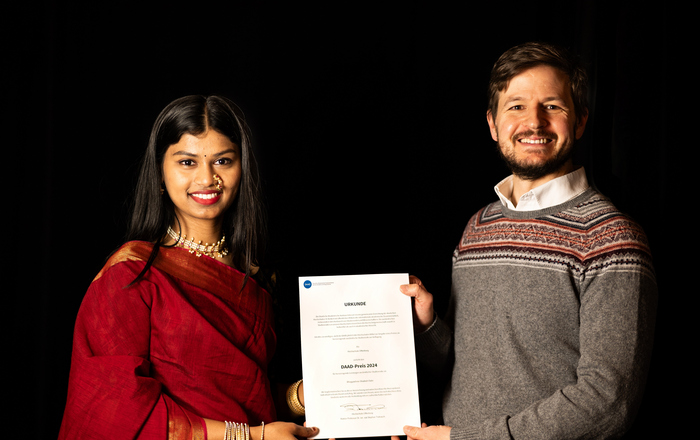 2024-11-26 PM International Evening und DAAD-Preisverleihung A woman in traditional Indian dress and a man in a woolen sweater hold a certificate