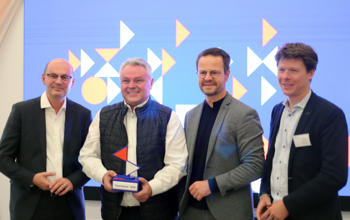 2025-10-23 PM Transferpreis Vier Männer stehen in einer Reihe, der Zweite von links hält einen Award in Händen