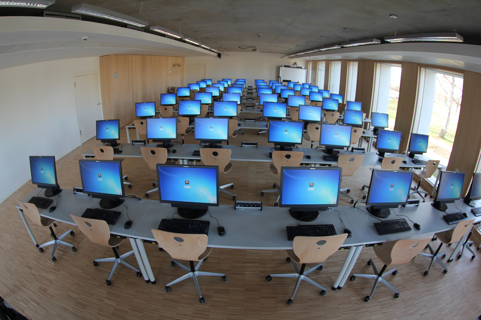 Ein menschenleerer Hörsaal mit ganz vielen eingeschalteten Computerbildschirmen.