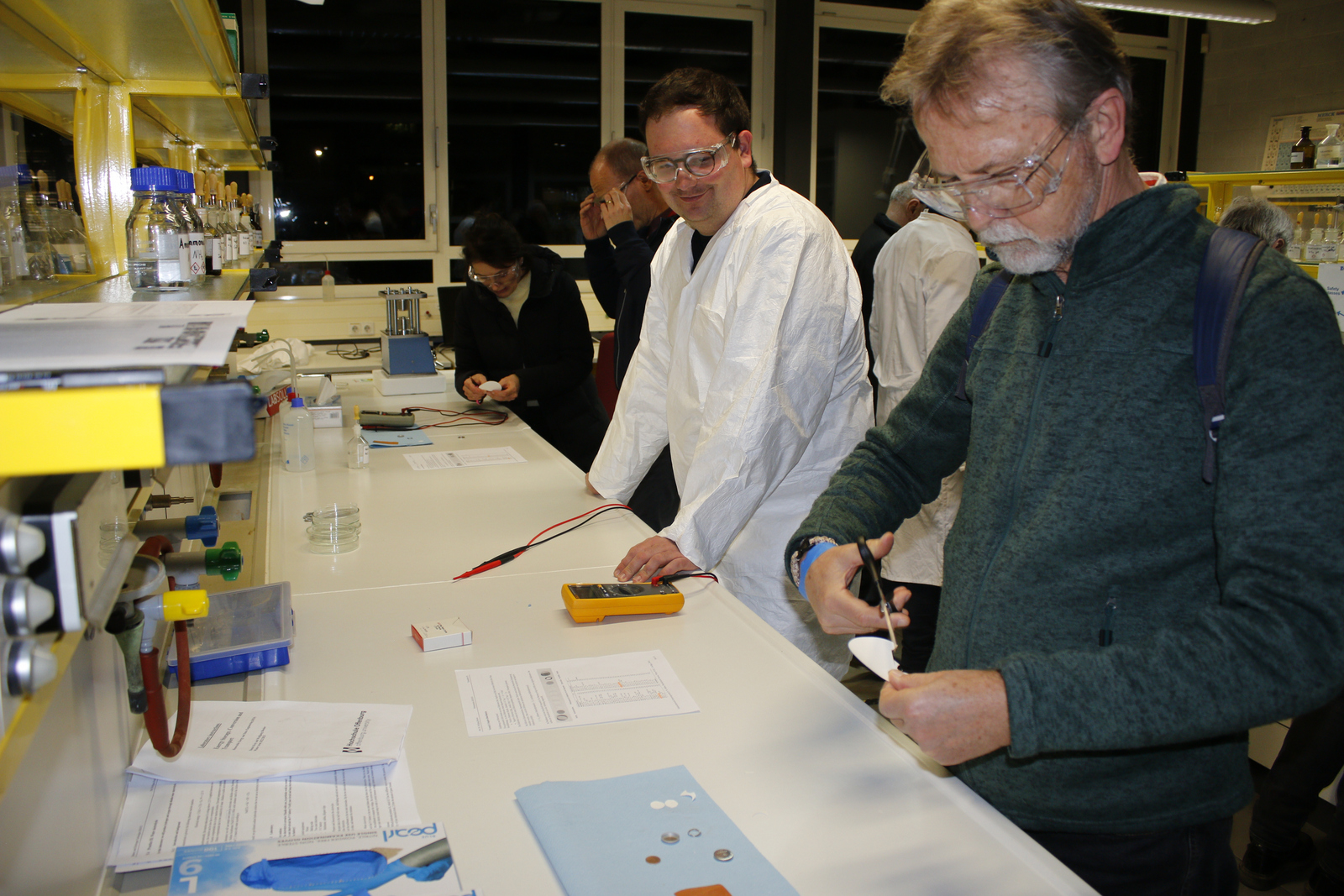 Ein junger Mann im weißen Kitteln unterstützt Besucherinnen und Besucher bei der Laborarbeit