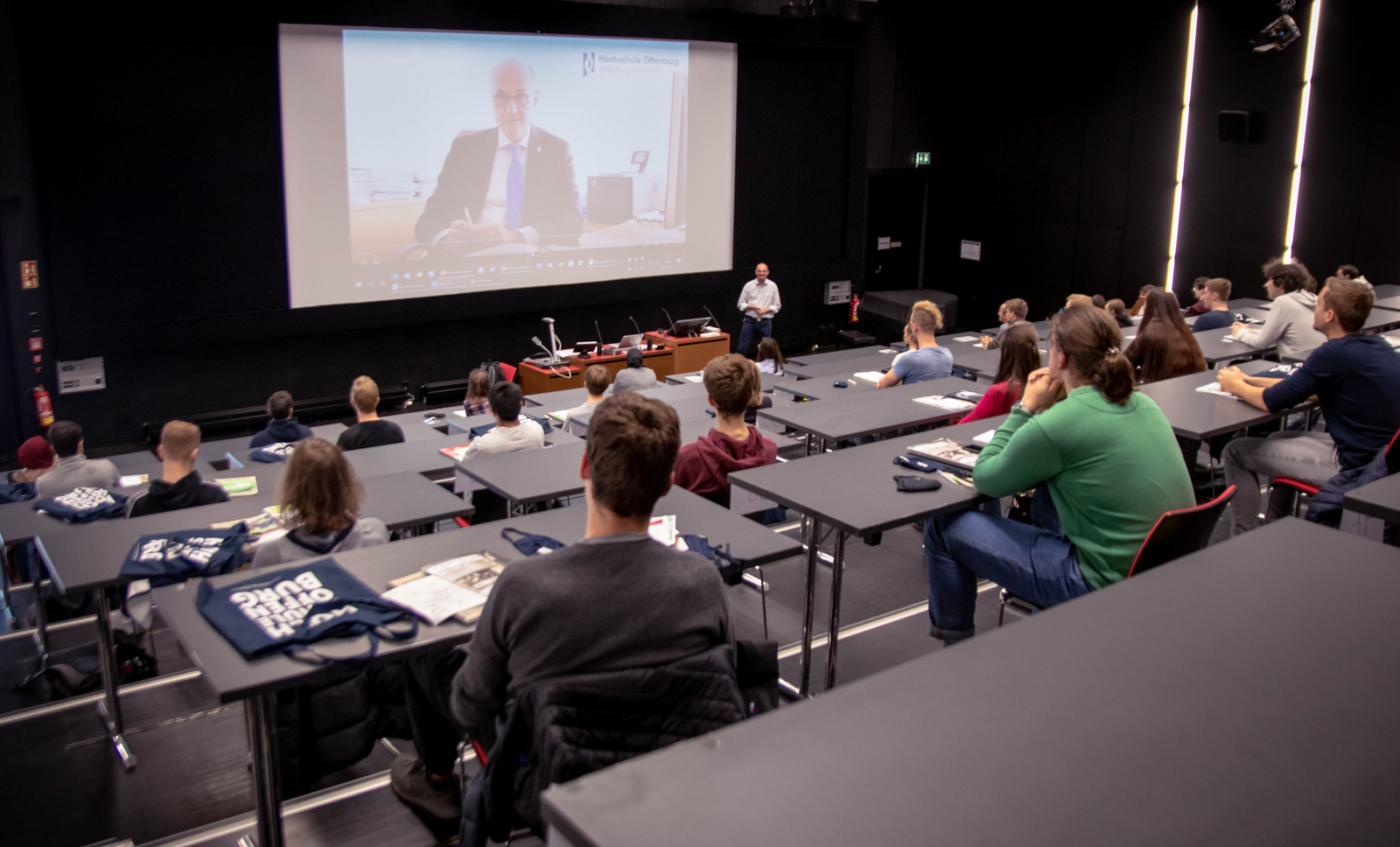 Hörsaal mit Erstsemestern zu denen Rektor Prof. Dr. Winfried Lieber von einer Videoleinwand spricht.