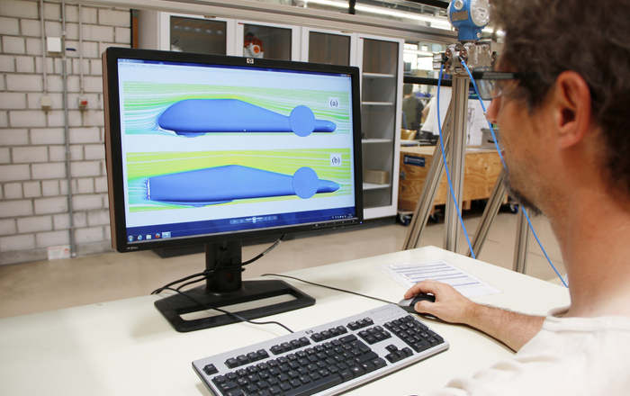 Ein Mann sitzt am PM, auf dem Bildschirm sind zwei unterschiedliche Fahrzeugdesigns und Strömungsverläufe grafisch dargestellt  