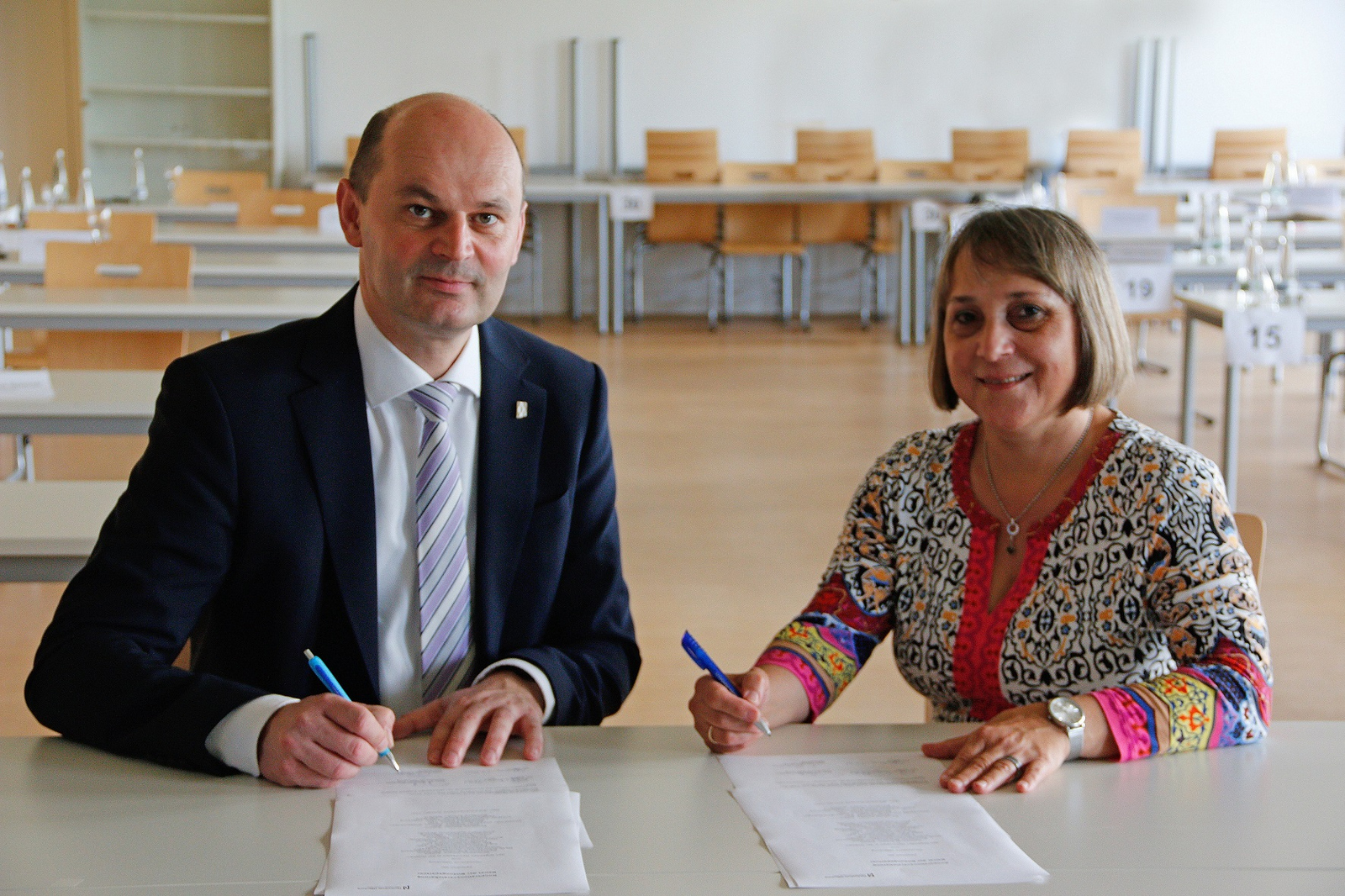 Rektor Prof. Dr. Stephan Trahasch (links) und Schulleiterin Claudia Cassiani (rechts) bei der Unterzeichnung der Partnerschaftsurkunde. 