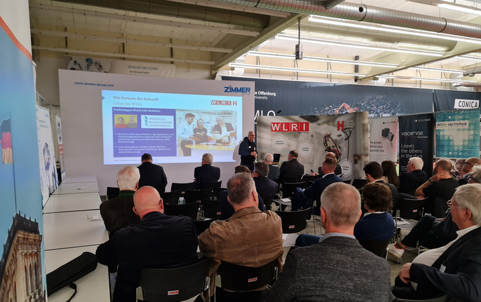 2025-10-15 PM Wirtschaftsrat Deutschland besucht WLRI Sitzende Menschen hören einem vor einer Leinwand stehenden Redner zu