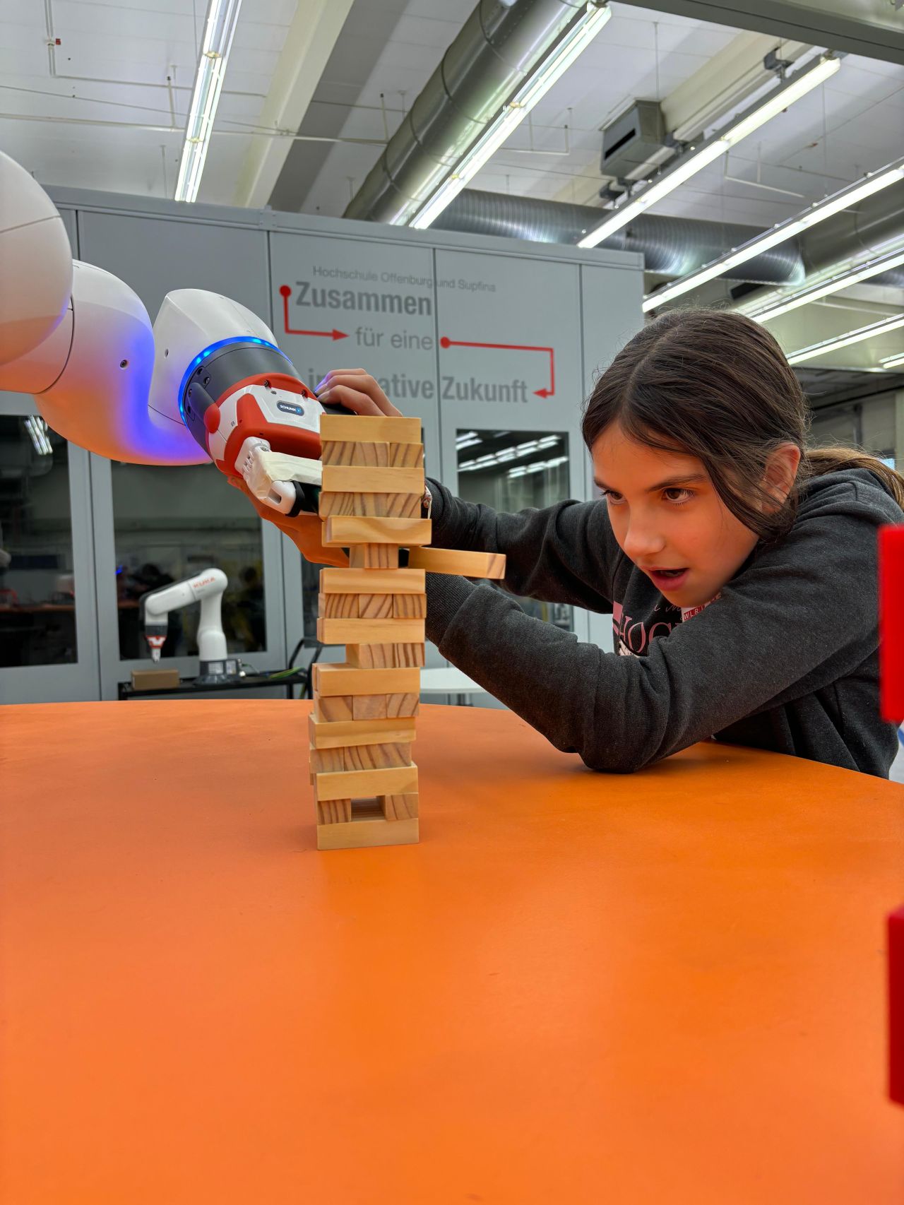 Ein Mädchen steuert einen Roboterarm, um Jenga mit Holzklötzen zu spielen