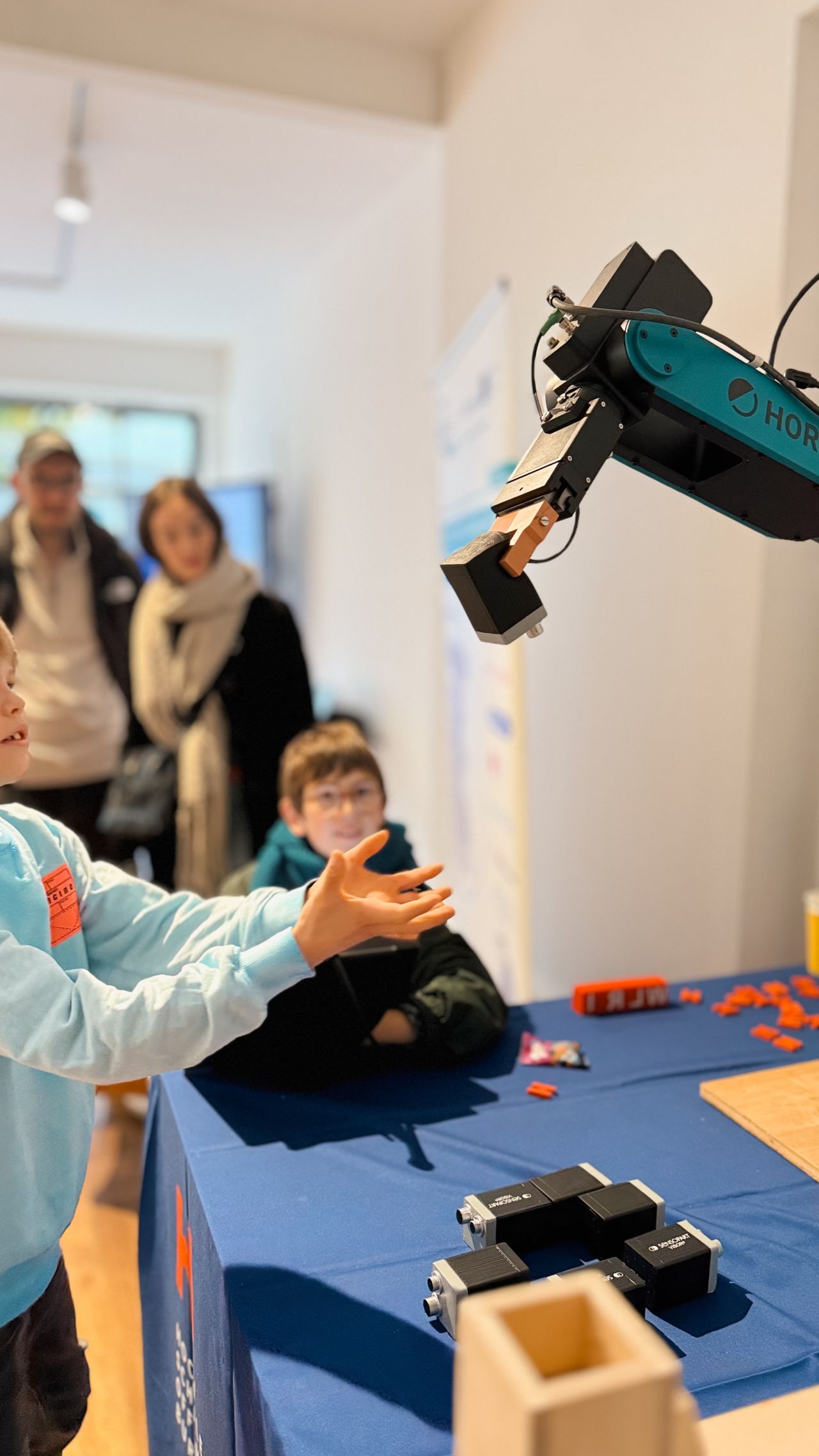 A young boy reaches towards a robot arm that is handing him a black cube