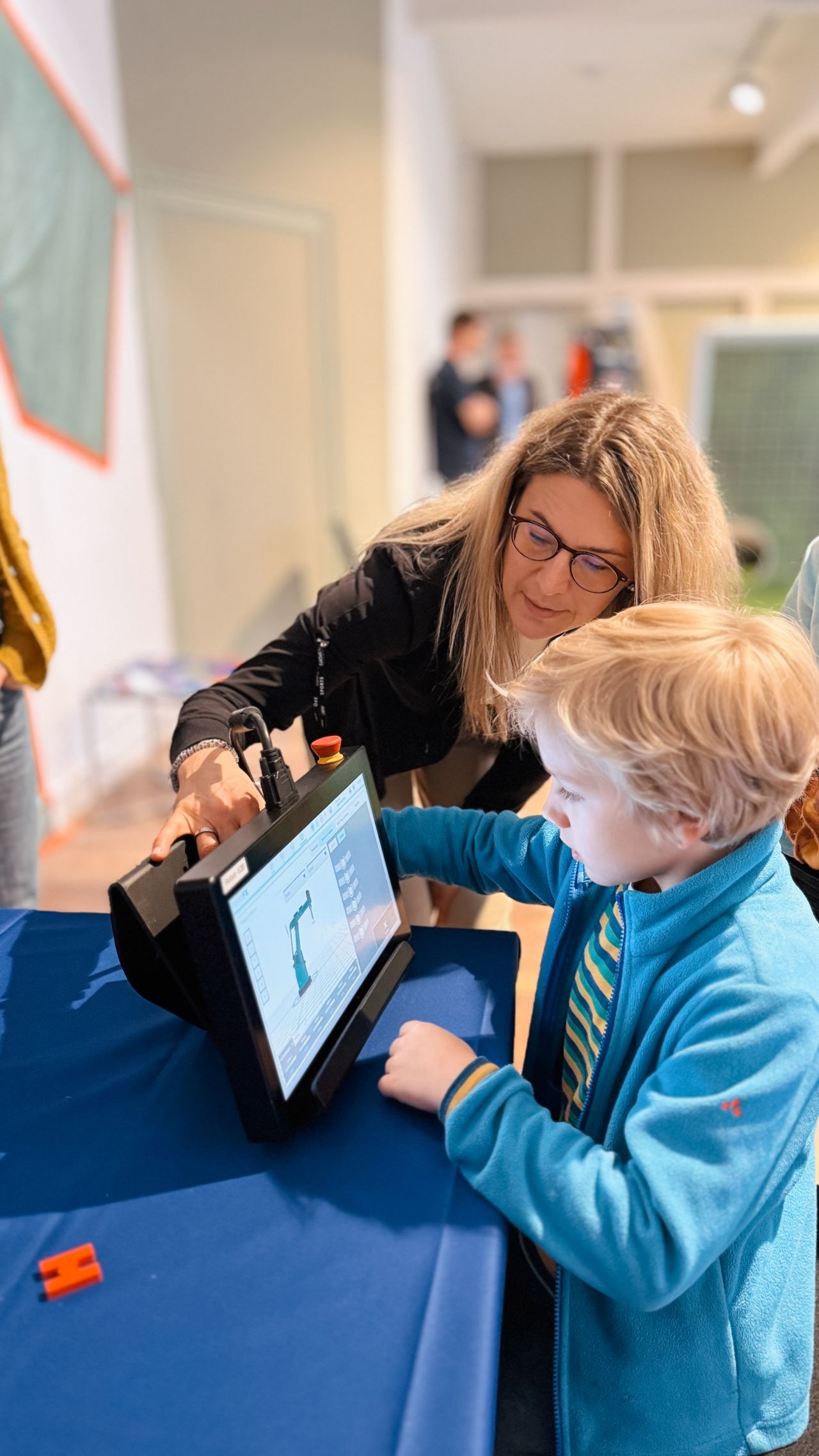 A woman shows a boy a tablet with a robot